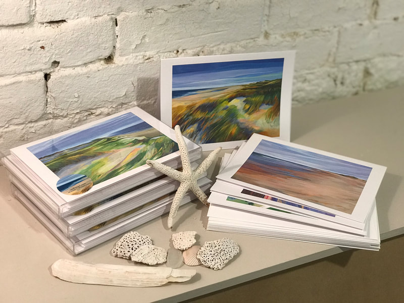 A picture shows various notecard boxes on display. Each notecard has a different image of a painting by Deidre Tao.