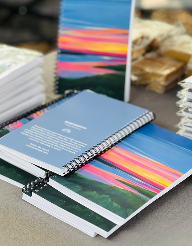 A picture shows several journals stacked together on display. The journal shows sunrise colors of peaches and pinks and yellows on a blue background. 