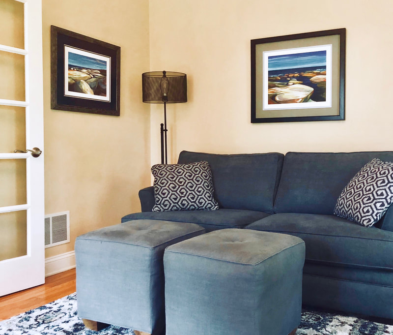 A contemporary interior home shows a blue sofa and cushions with two framed and matted prints of Deidre's artwork hanging nearby.